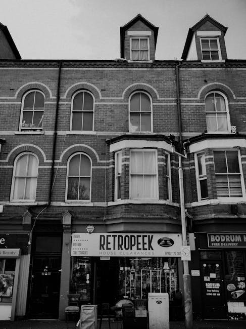 The image depicts the facade of a multi-story brick building with a ground-floor retail space. The upper floors feature several large, arched windows with white frames, set within the brickwork, and t
